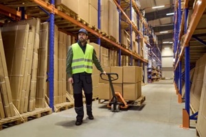 worker in warehouse pulls pallet with jack